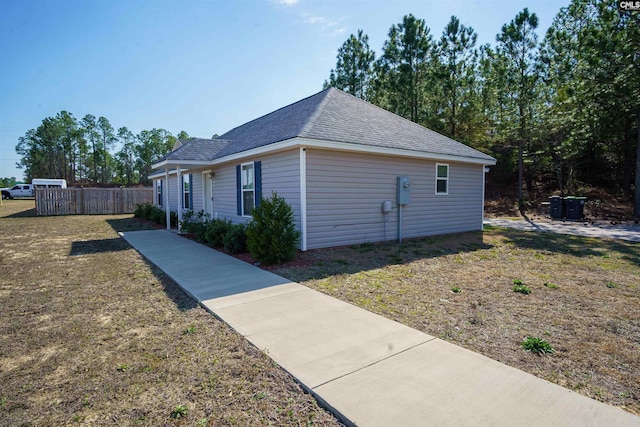 view of side of home featuring a shingled roof and fence