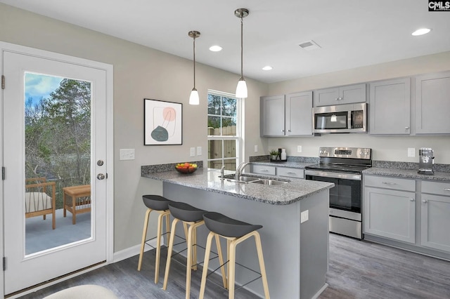 kitchen featuring gray cabinetry, a breakfast bar area, stainless steel appliances, a sink, and wood finished floors