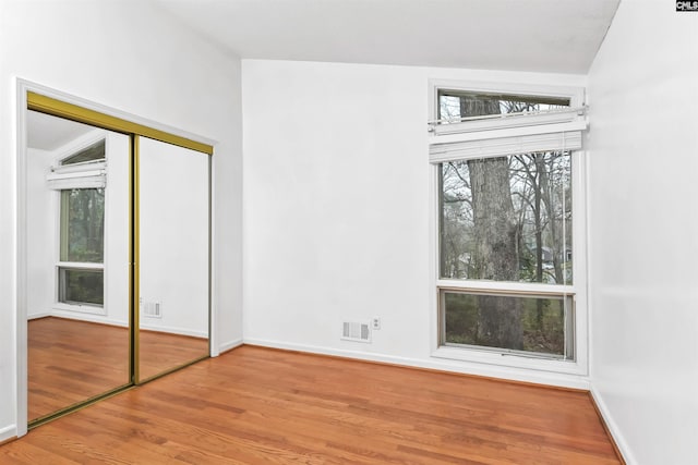 unfurnished bedroom featuring a closet, visible vents, baseboards, and wood finished floors