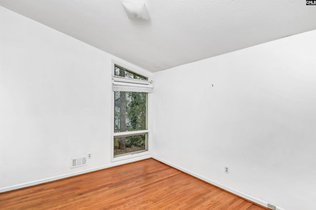 unfurnished room with vaulted ceiling, wood finished floors, visible vents, and baseboards