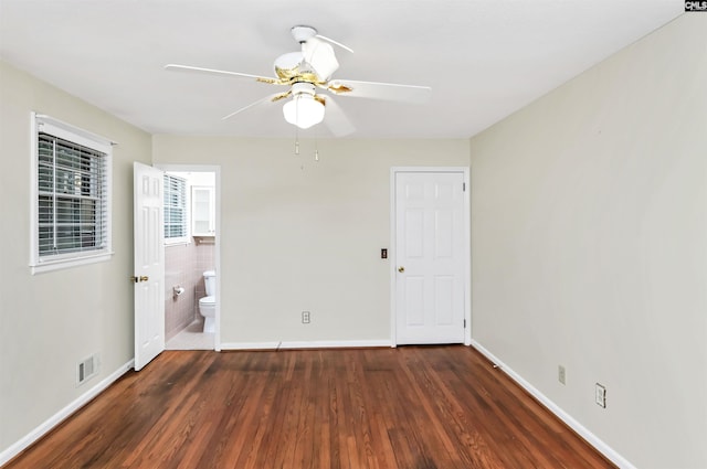 unfurnished bedroom featuring visible vents, a ceiling fan, ensuite bathroom, wood finished floors, and baseboards