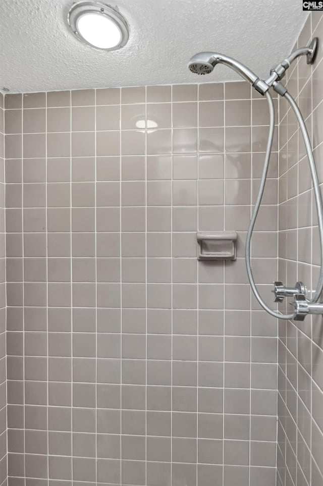 full bathroom featuring a tile shower and a textured ceiling