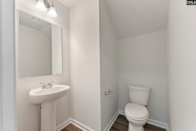 bathroom featuring visible vents, baseboards, toilet, wood finished floors, and a sink