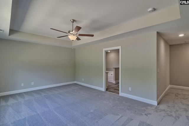 unfurnished bedroom featuring a raised ceiling, a ceiling fan, ensuite bath, carpet, and baseboards