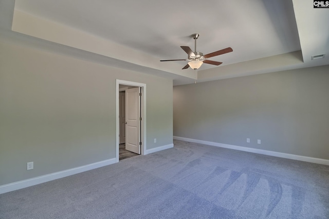 carpeted empty room featuring visible vents, a ceiling fan, a raised ceiling, and baseboards