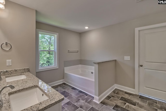 bathroom with a bath, double vanity, baseboards, and a sink