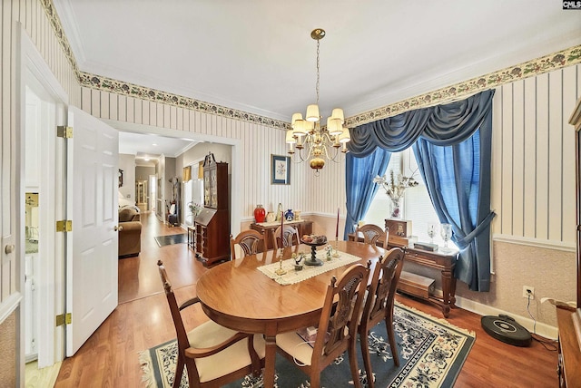 dining space featuring crown molding, wallpapered walls, light wood-type flooring, and an inviting chandelier