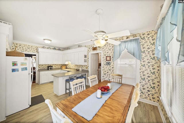 dining space featuring ceiling fan, light wood-style flooring, ornamental molding, and wallpapered walls