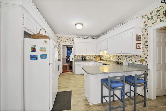 kitchen featuring wallpapered walls, crown molding, light wood-style flooring, a peninsula, and freestanding refrigerator