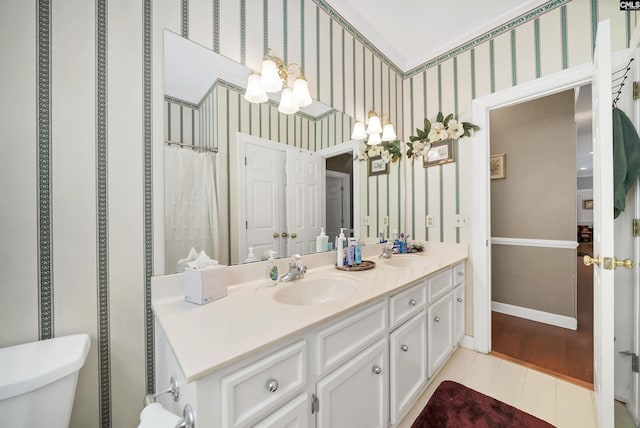 full bathroom with double vanity, wallpapered walls, baseboards, and a sink