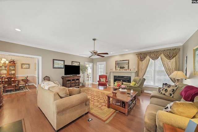 living area with a premium fireplace, baseboards, wood finished floors, and ornamental molding