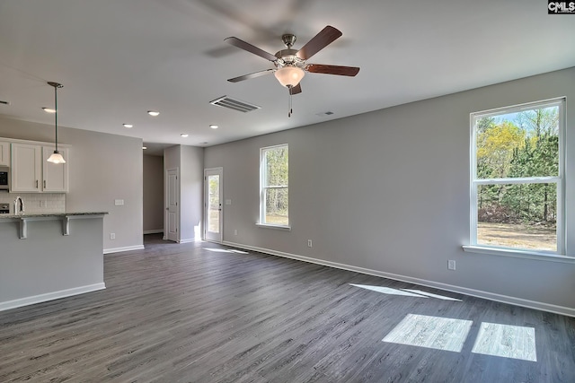 unfurnished living room featuring ceiling fan, visible vents, baseboards, and dark wood finished floors