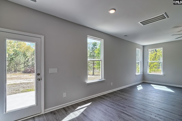 empty room with visible vents, a healthy amount of sunlight, dark wood-type flooring, and baseboards