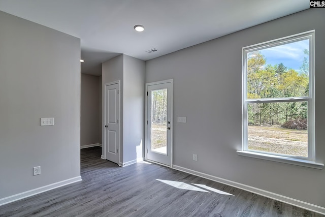 spare room featuring a wealth of natural light, visible vents, baseboards, and wood finished floors