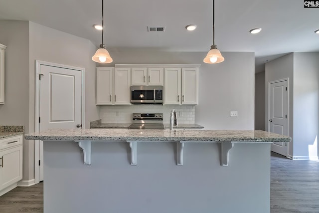 kitchen with tasteful backsplash, visible vents, appliances with stainless steel finishes, a kitchen breakfast bar, and white cabinets