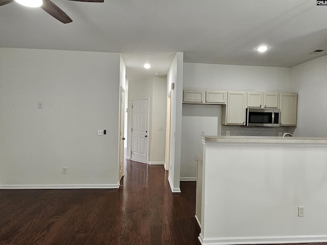 kitchen featuring stainless steel microwave, baseboards, dark wood-style floors, and decorative backsplash