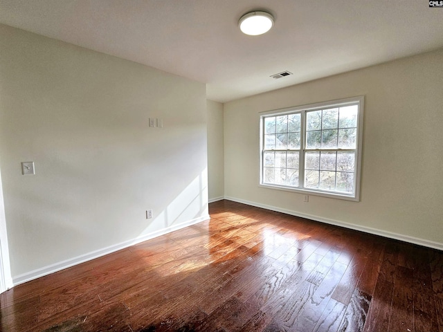 empty room featuring visible vents, wood-type flooring, and baseboards