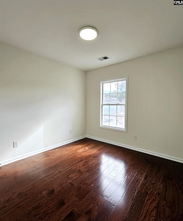 spare room with dark wood finished floors, visible vents, and baseboards