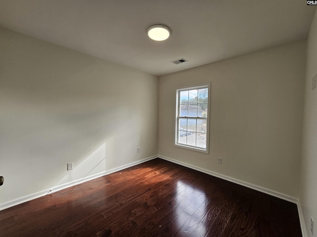 unfurnished room featuring dark wood finished floors, visible vents, and baseboards