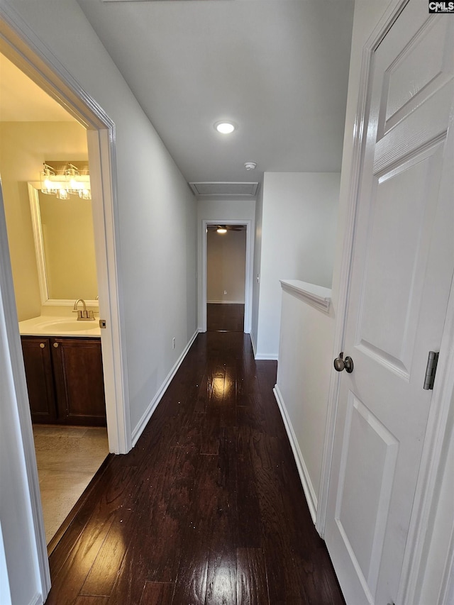 corridor featuring dark wood-style flooring, baseboards, and a sink