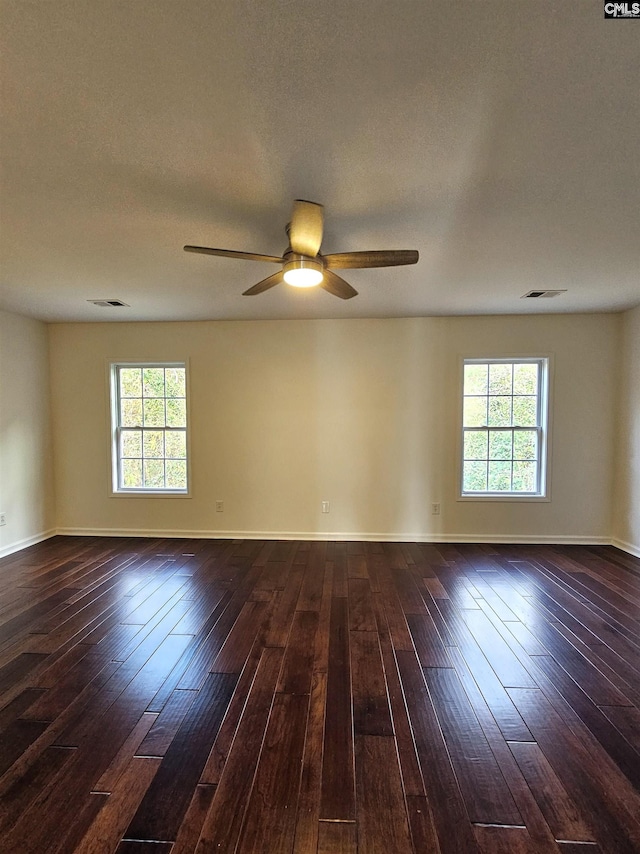 spare room with a wealth of natural light, visible vents, dark wood-type flooring, and ceiling fan