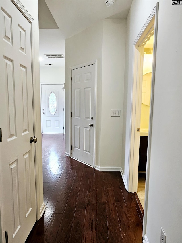 corridor featuring visible vents, baseboards, and dark wood-type flooring