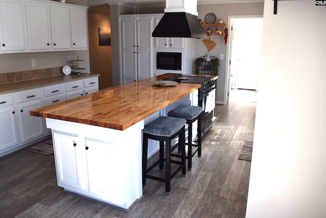 kitchen featuring island range hood, a kitchen island, black appliances, white cabinets, and butcher block counters