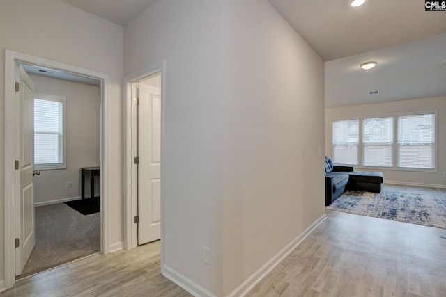 hallway with light wood finished floors, visible vents, and baseboards