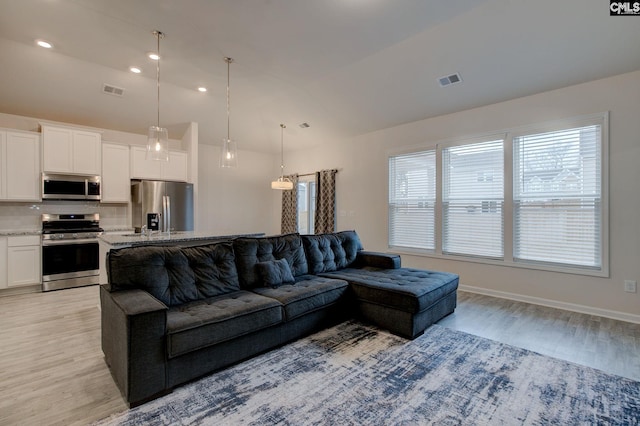 living room featuring visible vents, lofted ceiling, baseboards, and light wood-style flooring