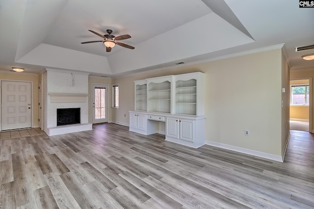 unfurnished living room featuring built in desk, visible vents, light wood finished floors, and a tray ceiling