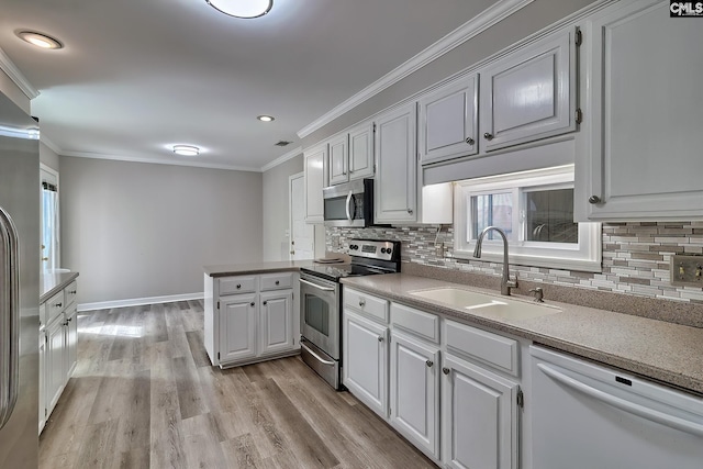 kitchen with a peninsula, crown molding, appliances with stainless steel finishes, and a sink