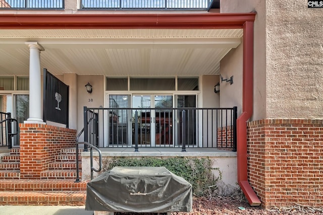 doorway to property with a porch, brick siding, and stucco siding