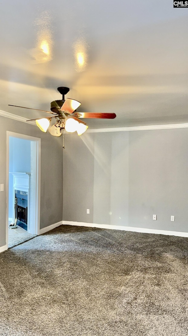 carpeted spare room with ornamental molding, a fireplace, baseboards, and ceiling fan