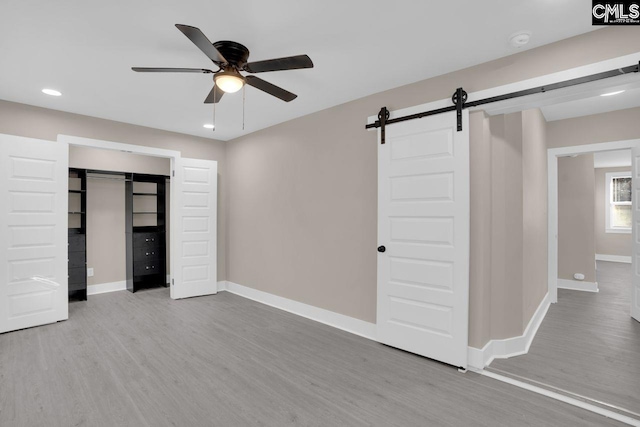 unfurnished bedroom with a ceiling fan, wood finished floors, recessed lighting, a barn door, and baseboards