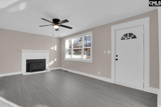 unfurnished living room featuring ceiling fan, a fireplace, baseboards, and dark wood-style flooring