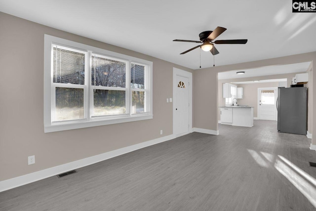 unfurnished living room with visible vents, ceiling fan, baseboards, dark wood-style floors, and a sink