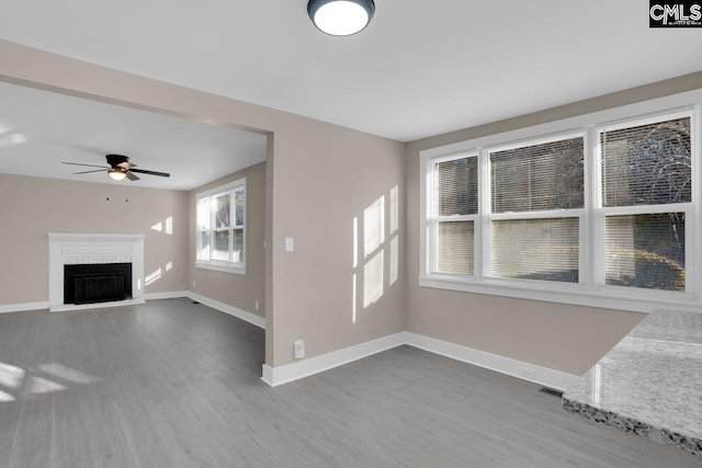 unfurnished living room with visible vents, a fireplace with raised hearth, a ceiling fan, wood finished floors, and baseboards