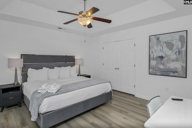 bedroom with a closet, visible vents, a tray ceiling, and wood finished floors