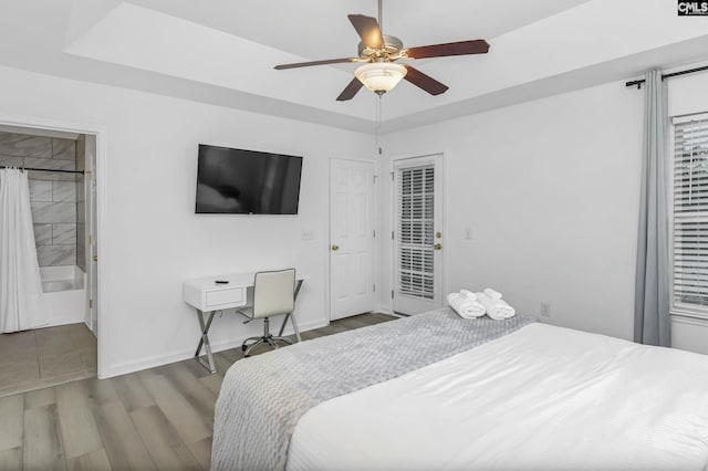 bedroom featuring ceiling fan, baseboards, a tray ceiling, wood finished floors, and access to outside