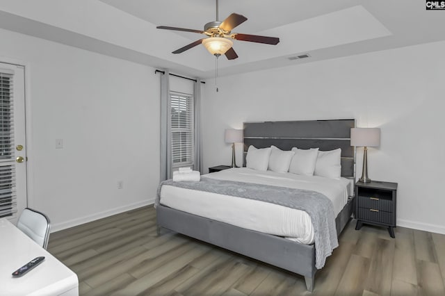 bedroom with visible vents, baseboards, a tray ceiling, wood finished floors, and a ceiling fan