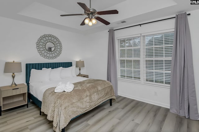 bedroom with a raised ceiling, wood finished floors, visible vents, and baseboards