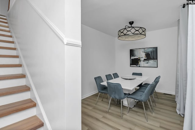 dining room featuring baseboards, light wood-style flooring, and stairs