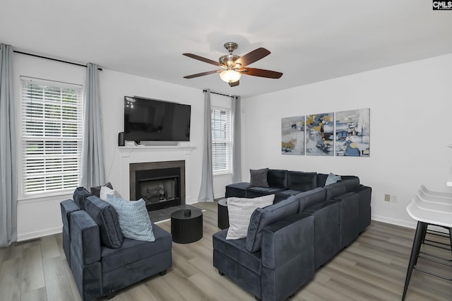 living room featuring a fireplace, a ceiling fan, baseboards, and light wood finished floors