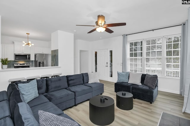 living area featuring baseboards, ceiling fan with notable chandelier, and light wood finished floors