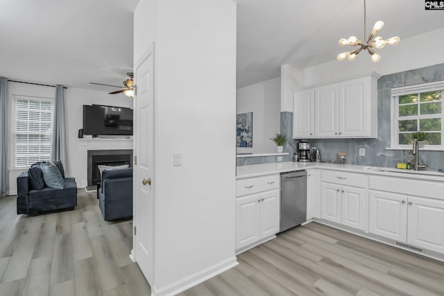 kitchen with light wood-type flooring, a sink, a fireplace, light countertops, and dishwasher