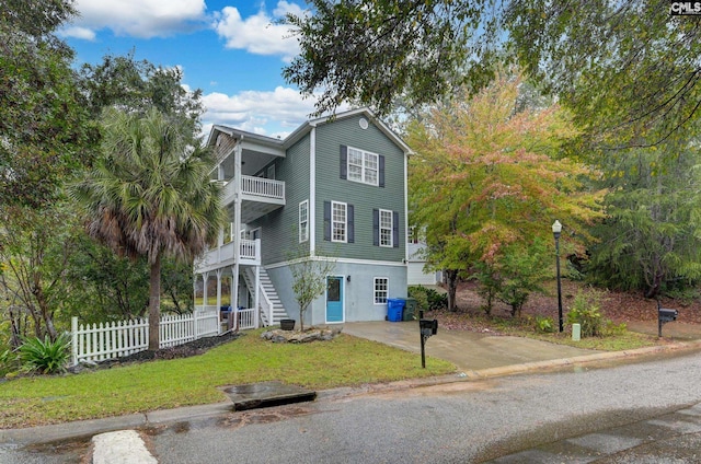 view of front of home with a front lawn, a balcony, stairs, and fence