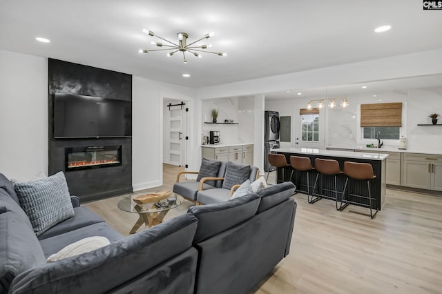 living area featuring a barn door, stacked washer / dryer, a notable chandelier, and light wood finished floors