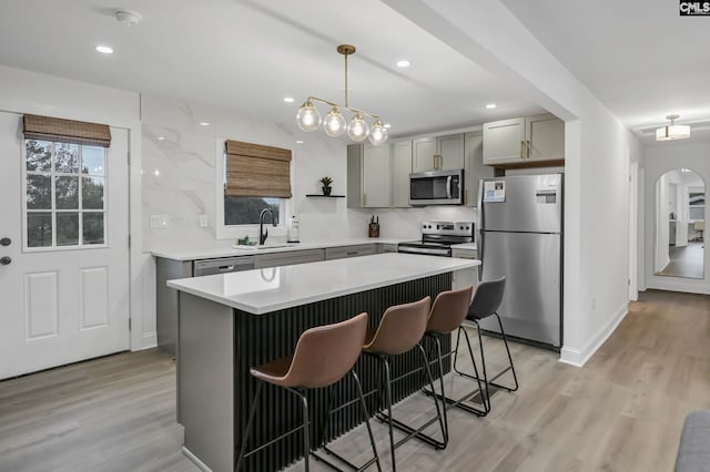 kitchen with light wood-type flooring, gray cabinets, appliances with stainless steel finishes, arched walkways, and a sink