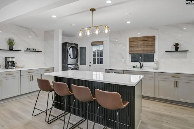 kitchen featuring open shelves, a sink, stacked washer and clothes dryer, a kitchen bar, and a center island