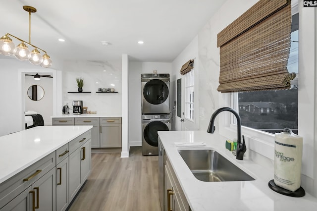 kitchen with open shelves, a sink, gray cabinetry, light countertops, and stacked washer / dryer